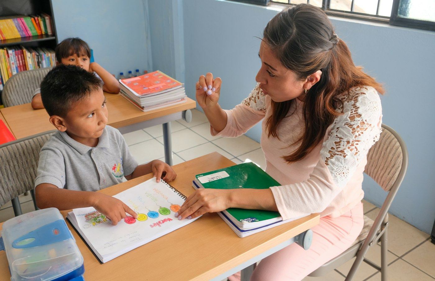 A teacher guiding a young student with her notebook